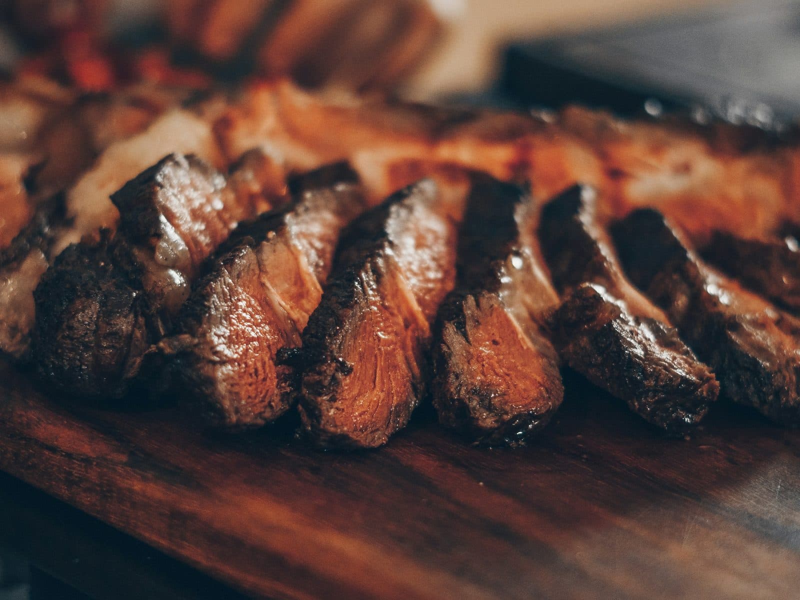 A sliced, rested steak on a wooden board in warm low light
